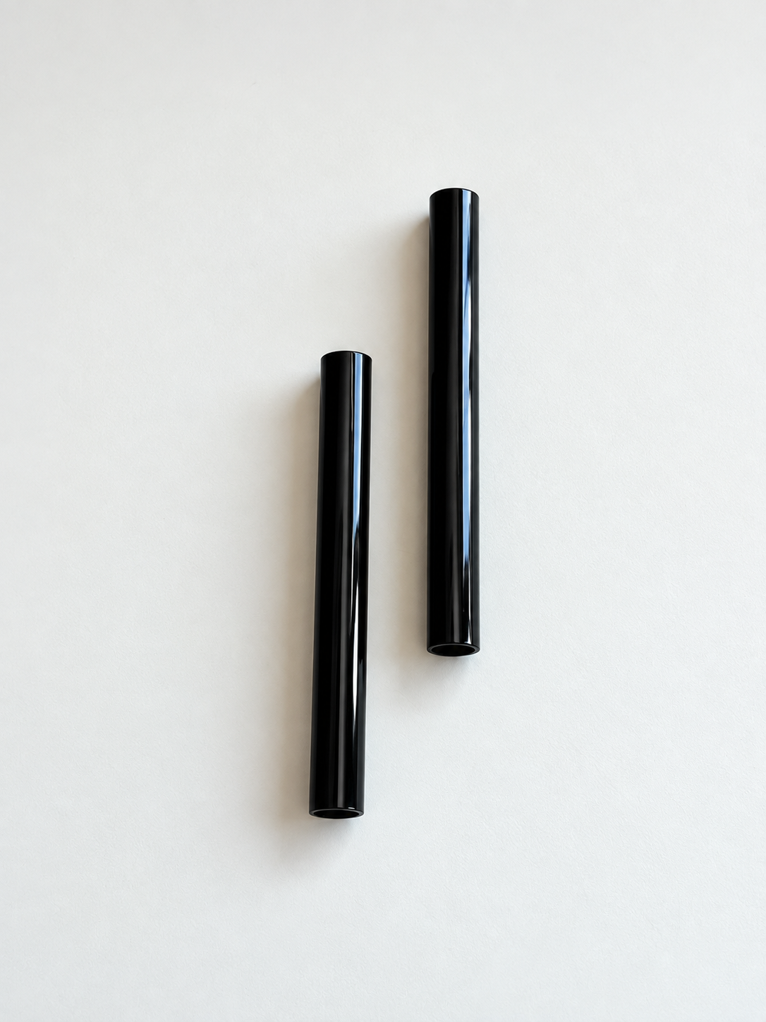 Zwei glänzend schwarze Aluminiumröhrchen, senkrecht und leicht versetzt auf hellem Hintergrund angeordnet.