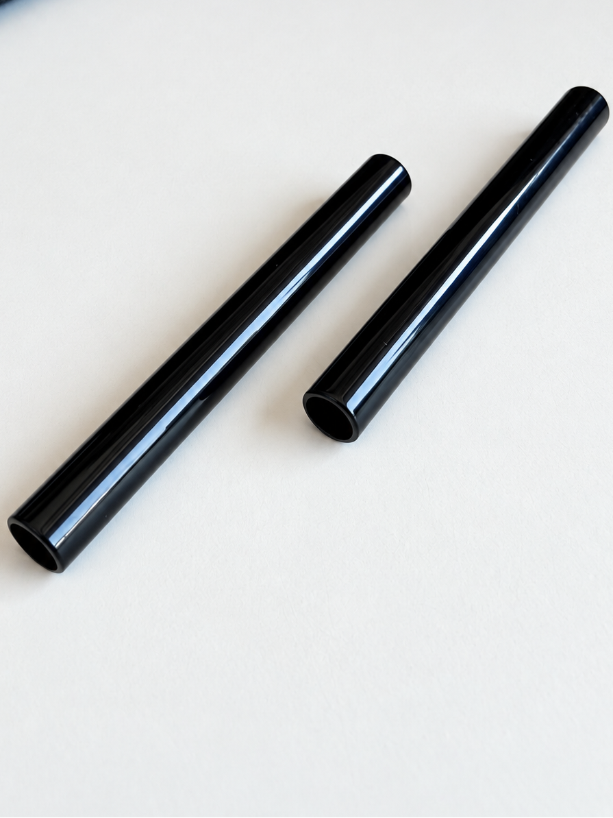 Zwei glänzend schwarze Aluminiumröhrchen liegen diagonal nebeneinander auf hellem Hintergrund.