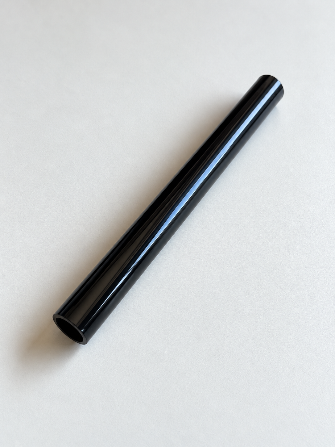 Ein glänzend schwarzes Aluminiumröhrchen liegt diagonal auf hellem Grund; die runde Öffnung ist sichtbar.