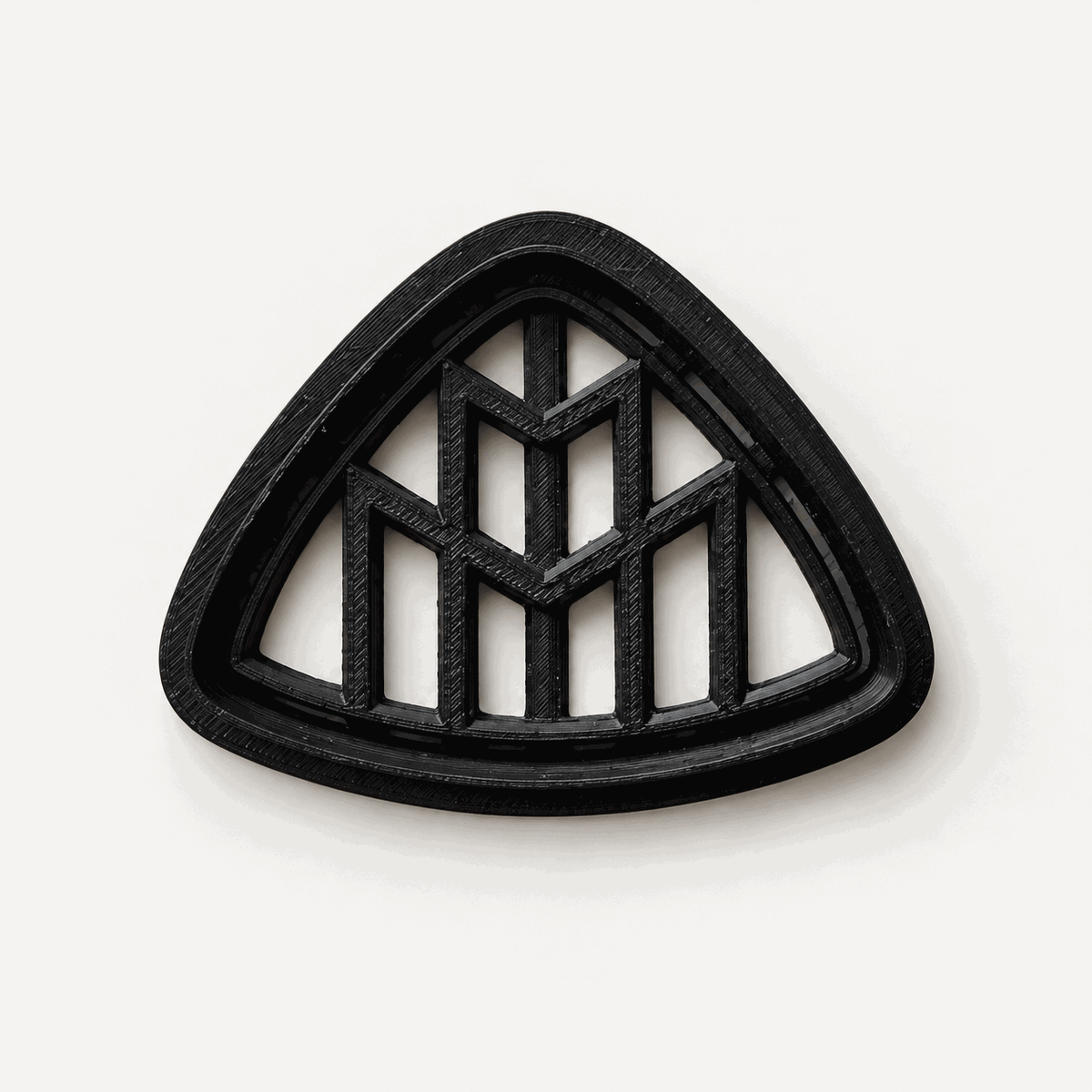 Schwarzer dreieckiger Keksausstecher mit geometrischem Maybach-Doppel-M-Motiv auf hellem Hintergrund.