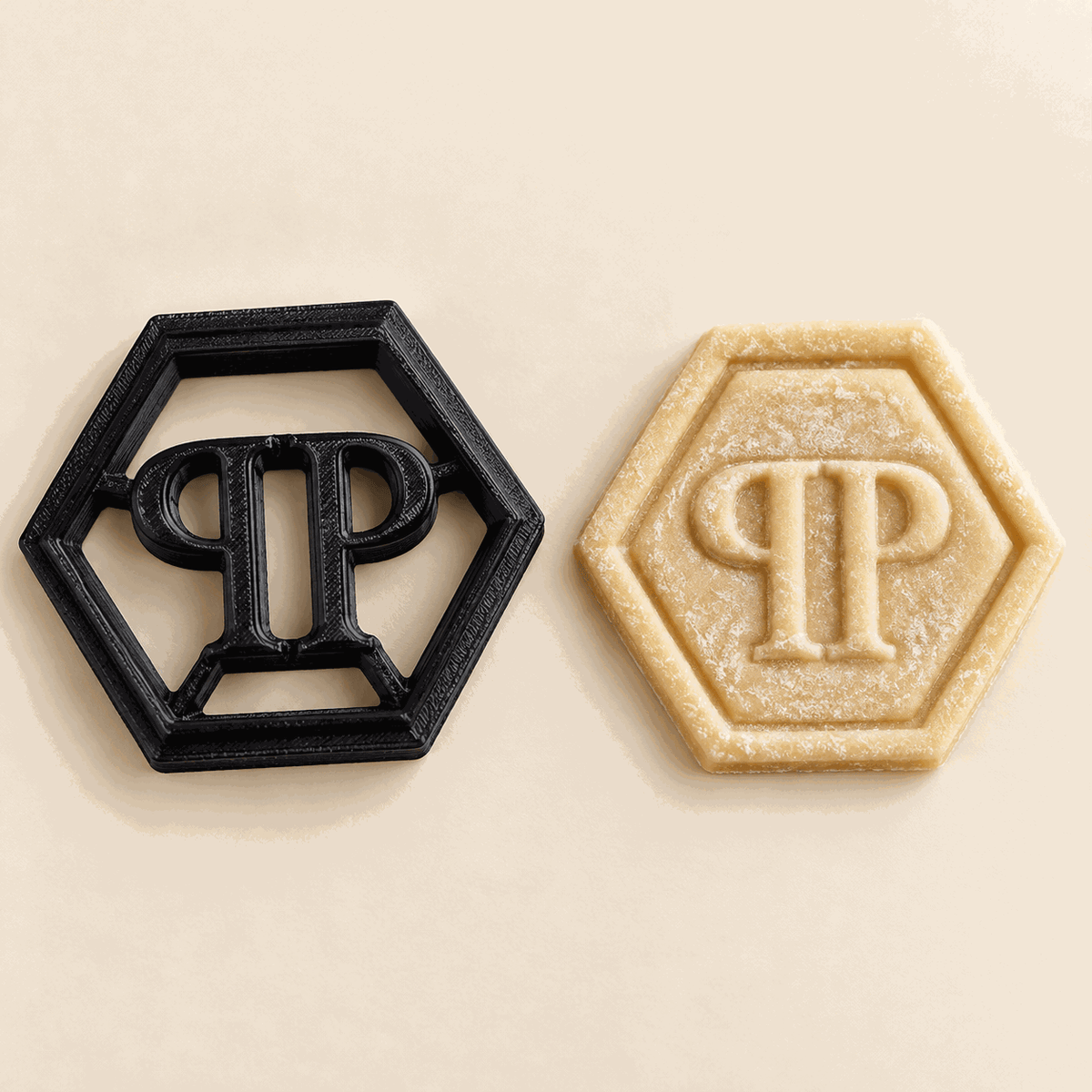 Schwarzer sechseckiger PP-Keksausstecher neben einem Keks mit geprägtem PP-Monogramm.