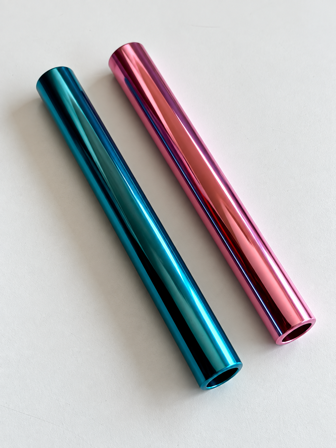 Blaues und pinkes glänzendes Aluminiumröhrchen, parallel und diagonal auf hellem Hintergrund angeordnet.