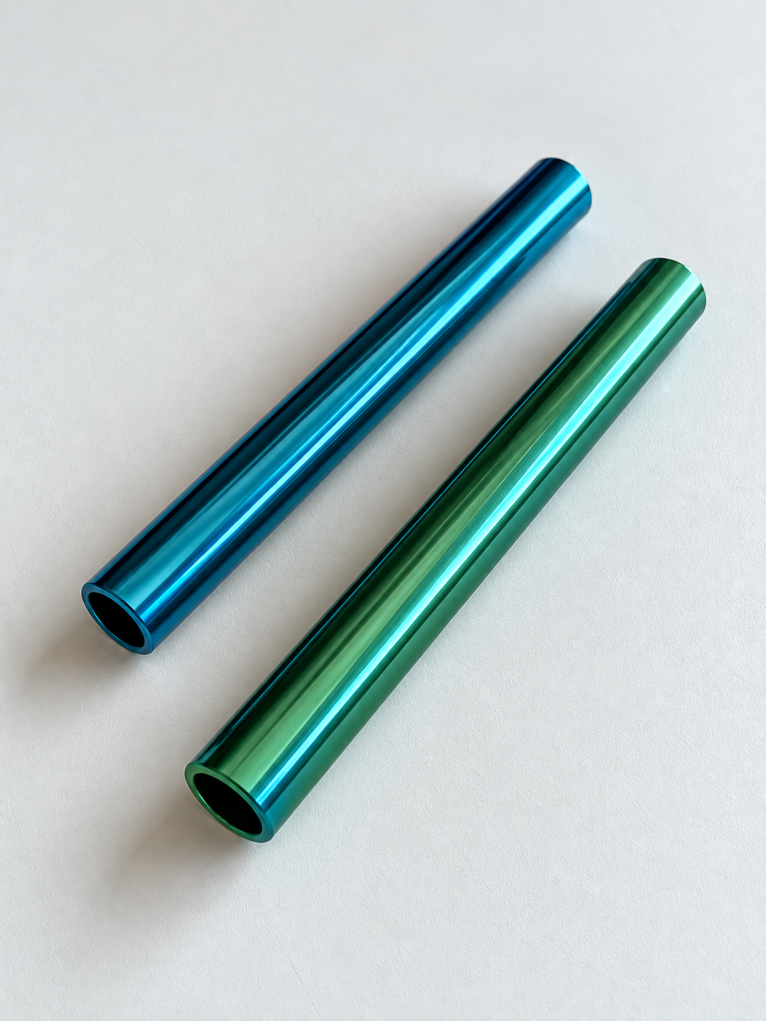 Blaues und grün-türkises Aluminiumröhrchen liegen diagonal auf hellem Grund, mit sichtbaren Öffnungen.