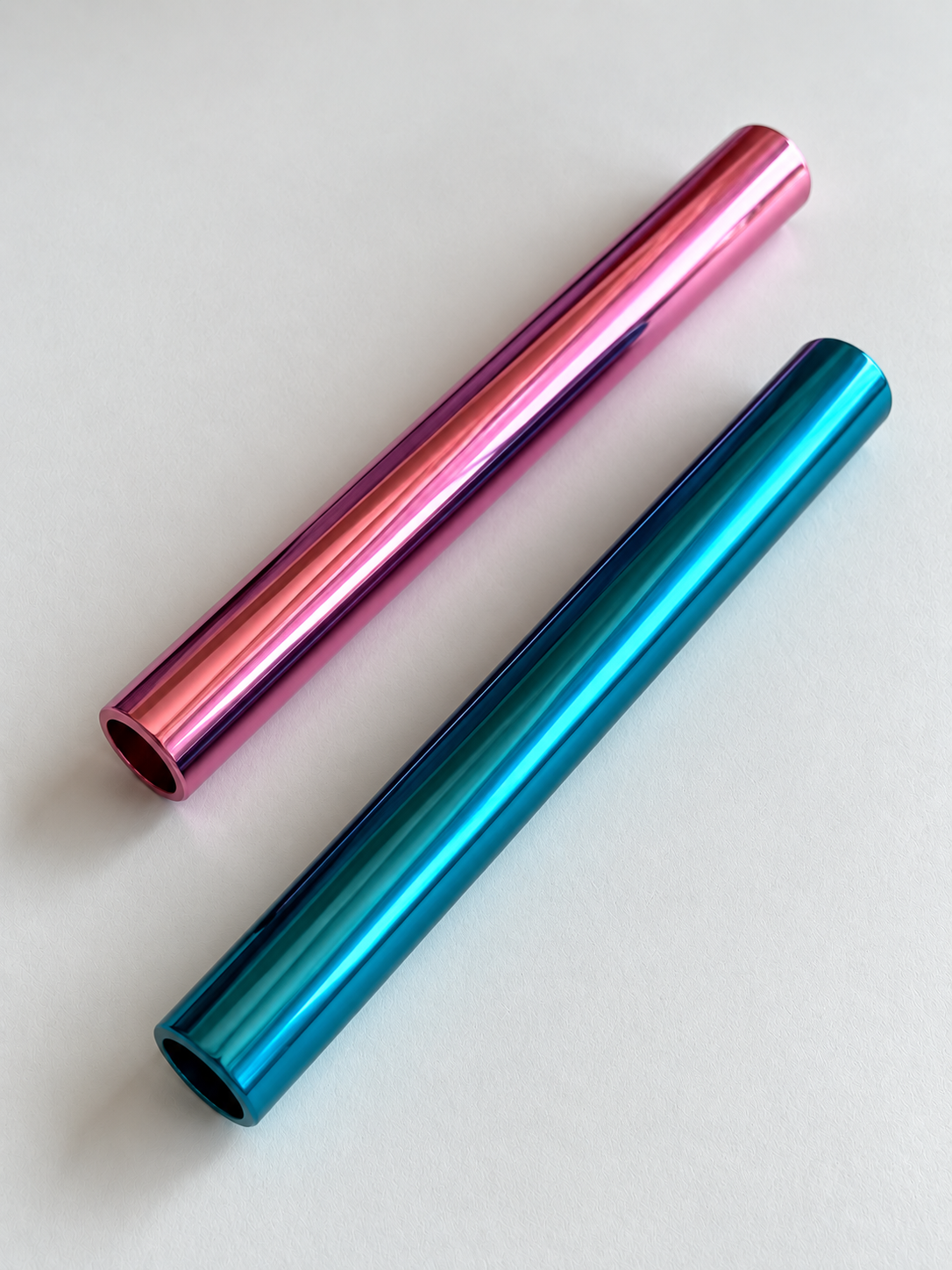 Pinkes und blaues Aluminiumröhrchen liegen diagonal auf hellem Grund, mit sichtbaren runden Öffnungen.