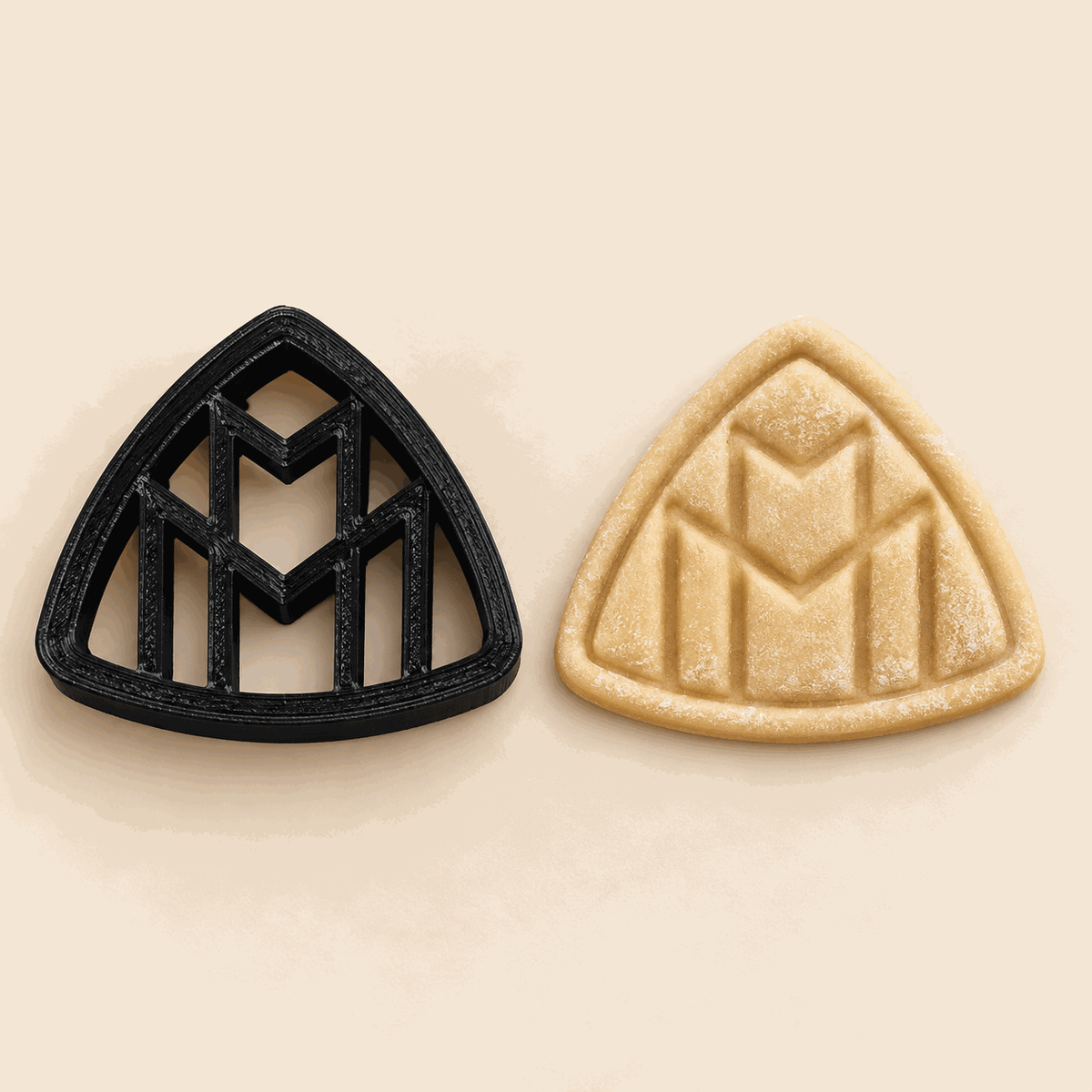 Schwarzer Maybach-Keksausstecher neben einem Keks mit geprägtem Doppel-M-Motiv.