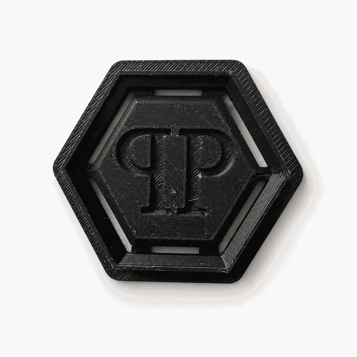 Schwarzer sechseckiger Keksausstecher mit PP-Monogramm auf hellem Hintergrund.