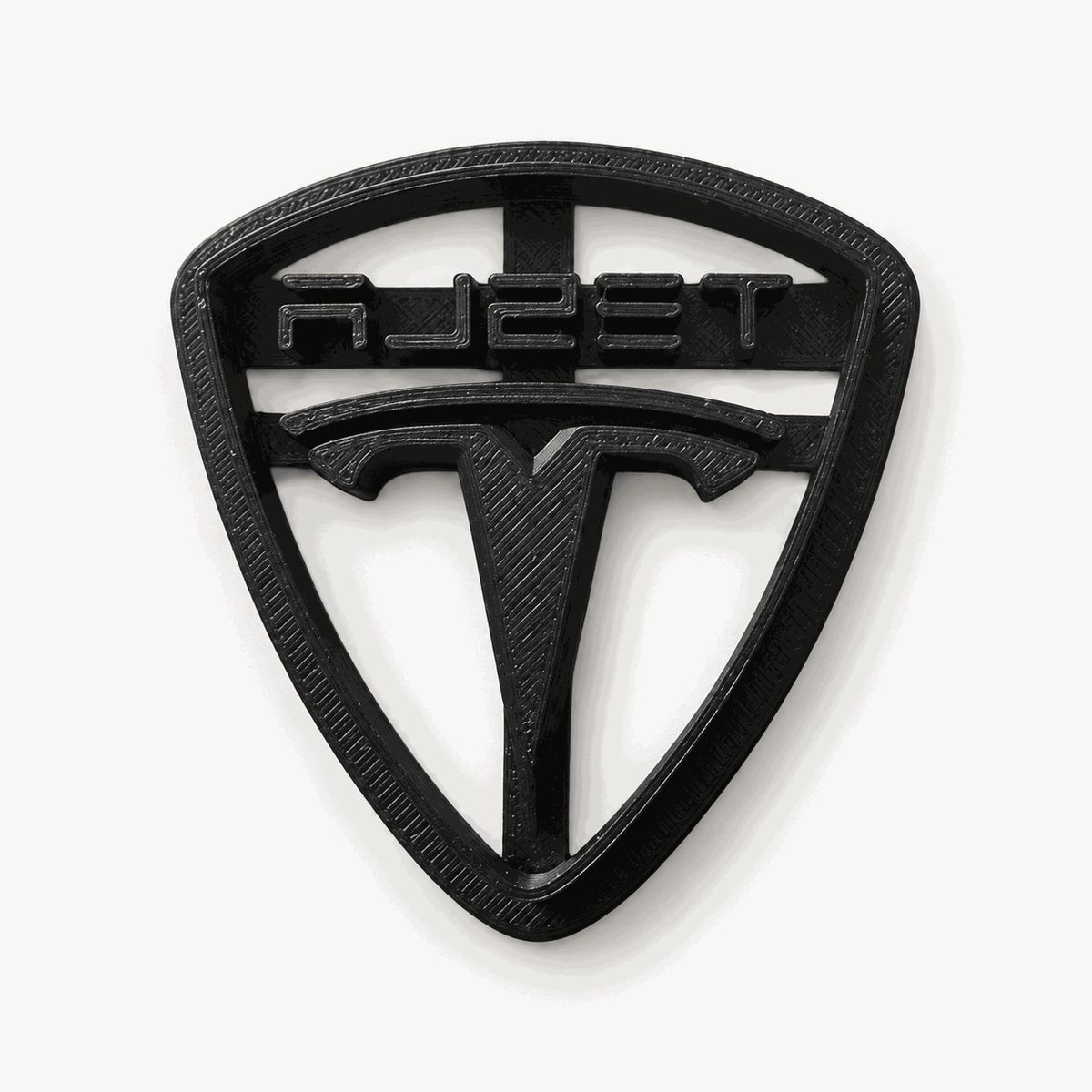 Schwarzer dreieckiger Keksausstecher mit Tesla-Schriftzug und T-Motiv auf hellem Hintergrund.