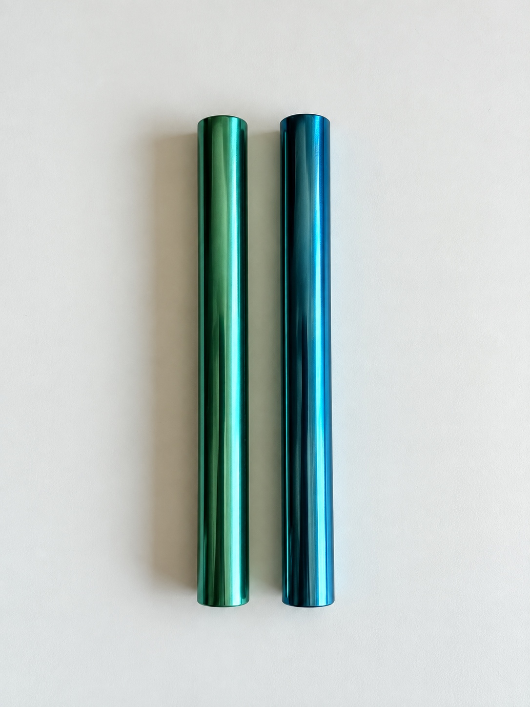 Grün-türkises und blaues glänzendes Aluminiumröhrchen, senkrecht nebeneinander auf hellem Hintergrund.